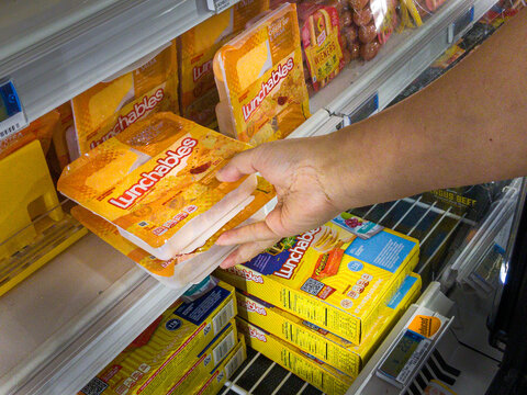 Shiloh, IL--July 10, 2021; Hand Of Shopper Reaching Into Refrigerator Section Of Grocery Store Selecting Two Oscar Meyer Lunchable Packages, A Kraft-Heinz Brand Of Food.