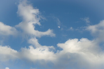 Blue sky evening with clouds rolling in. Moon peeking through the clouds.