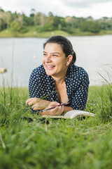 Hermosa mujer caucásica leyendo un libro en una zona verde a la orilla de un lago