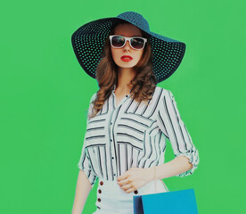 Portrait of beautiful young woman with shopping bags wearing a black round summer hat, white striped shirt on green background