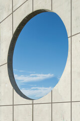 circular gap in a stone wall in a park through which you can see a sky with clouds