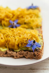 Home made avocado toasts with curried sauerkraut, garnished with boretch flowers.
