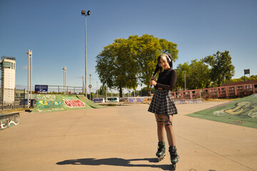 Cute young girl with heterochromia and punk style with white headphones and inline skates holding...