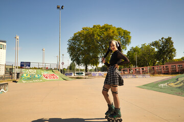 Young and beautiful girl with heterochromia and punk style with white headphones and inline skates holding a ponytail with both hands looking at the camera smiling.