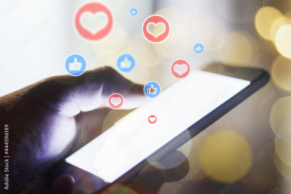 Aufkleber close up of hand holding white smartphone with glowing like icons on blurry background. social media