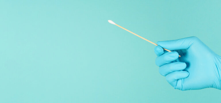 One Cotton stick for swab test in hand with blue medical gloves or latex glove on mint green or Tiffany Blue background.covid-19 concept. close up