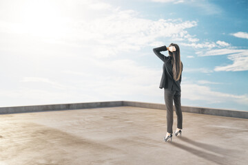 Thoughtful young businesswoman standing on building roof on beautiful sky background with mock up place for your advertisement. Success and future concept.