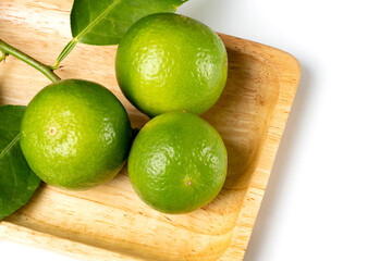 Close up natural fresh lime, green leaf, on wooden dish, white background.