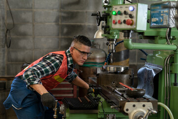 Caucasian engineer in reflective vest, safety glasses operating CNC milling machine at manufacturing workshop. Professional worker working in lathe machine at metal industry factory on a business day 