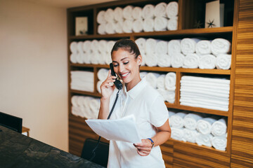 Beautiful young woman working at hotel in spa department and talking on phone. - obrazy, fototapety, plakaty