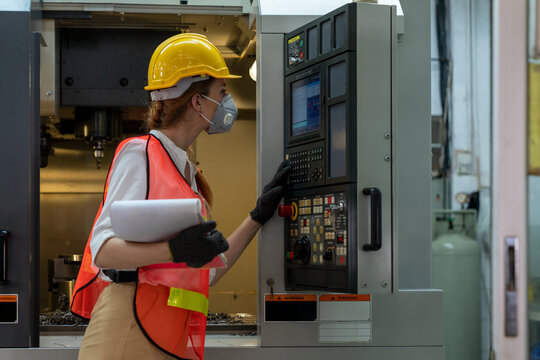 Portrait of female technician engineer control machines in the factory on a business day. Confident worker wearing particulate respirator mask with hard hat. Concept of Industrial manufacturing.