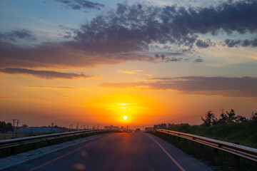 Fototapeta na wymiar Dawn on the road. The bright sun rises against the orange sky. Morning landscape