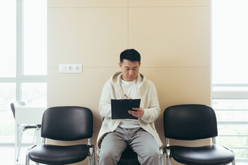 young asian male in waiting room for interview or meeting holding paper while sitting at chair fills out a resume questionnaire in office