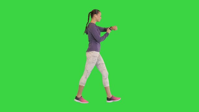 Sporty woman with wireless ear buds looking at the screen of a smart watch while walking on a Green Screen, Chroma Key.