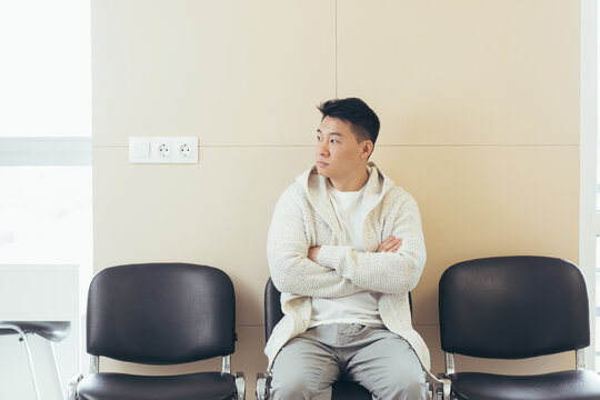 young asian man waiting for an interview or meeting sitting in the hallway in the waiting room. Student or entrant in the reception for exam or employment hr. Male patient in office a hospital clinic