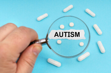 A man looks through a magnifying glass at pills and a leaf with the inscription - AUTISM