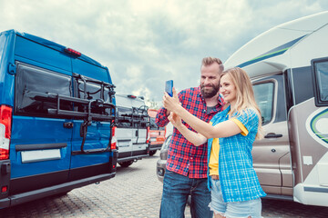 Woman and man taking selfie in front of RV or camper van in anticipation