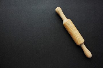 A rock for a test made of wood on a black background. Cooking and baking. cookery. View from above. Copy space. The scayple for the test is crushed on the right.