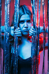 Fototapeta na wymiar Boring party. Lonely woman. Bad birthday. Unhappy celebration. Depressed lady black dress curly hair looking through shimmering cascade curtain blue red neon light.