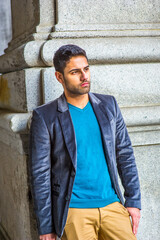 Dressing in a dark purple woolen blazer and blue sweater, a young handsome guy with bread and mustache is standing outside into deeply thinking..