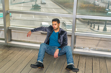 Against a glass wall, a young guy with beard and mustache is sitting on the floor into deeply...