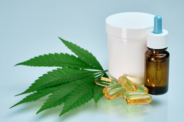 Bottle with CBD oil, cream, tablets and cannabis leaf on the blue background.