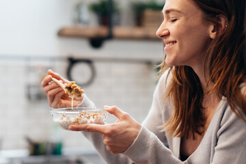 Young woman at home eating granola in the kitchen