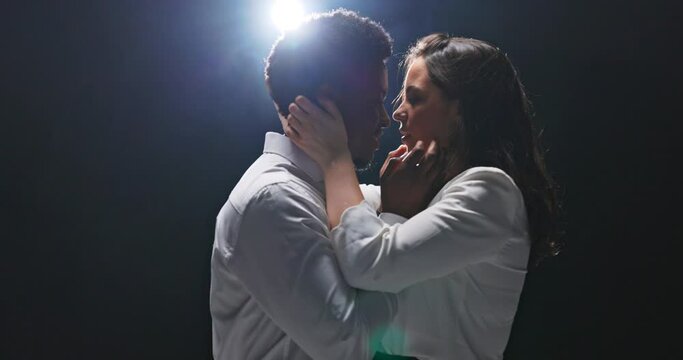 Romantic scene, partners approaching each other, grasping hands, man's hands on woman's cheeks, girl's hands on boyfriend's face, tender greeting, love, deep looks in eyes, dark background lit by lamp