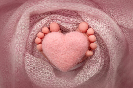 Feet of a newborn with a wooden heart, wrapped in a soft blanket. pink heart