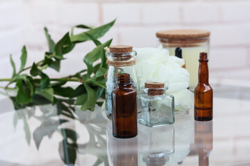 Little glass transparent and brown bottles with essential oil , white flower, herbs, white candle in a glass on glass table on white background. Aromatherapy, spa design