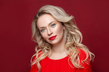 Friendly blonde woman with makeup and healthy curly hair smiling on red banner background