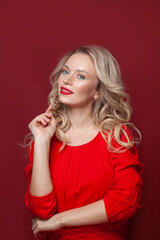 Perfect mature blonde woman with makeup and healthy curly hair wearing red dress on red banner background, portrait