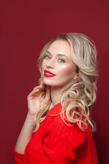 Cute woman with make up and blonde curly hair smiling on red background