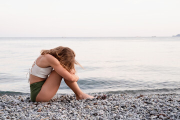 Fototapeta na wymiar young depressed woman sitting on the beach looking away, rear view