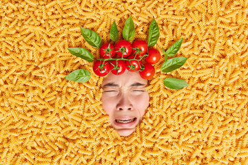 Upset dejected Asian woman cries unhappily has frustrated look buried in uncooked macaroni poses...
