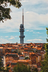 czech tv tower under bright blue sky with brown roof of old houses