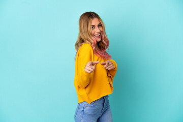 Young woman over isolated blue background surprised and pointing front
