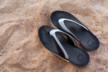 Fototapeta na wymiar Men's beach shoes on the sand. Black flip-flops