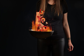 Shrimp tails and vegetables hovering in fire over wok pan in female hands