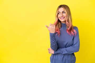 Young woman over isolated yellow background pointing to the side to present a product