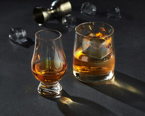 Two glasses of amber whiskey with ice on dark background