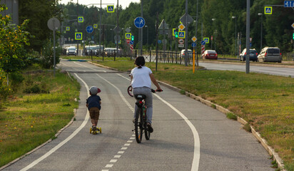 Mom and child ride a bicycle and scooter on a bike path in the city, family bike ride, active recreation, city life