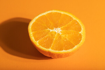 Fototapeta na wymiar Ripe cut orange on orange pastel background. Side view, close up, hard light.