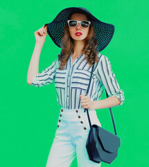 Portrait of beautiful elegant young woman wearing a black round summer hat, white striped shirt on green background