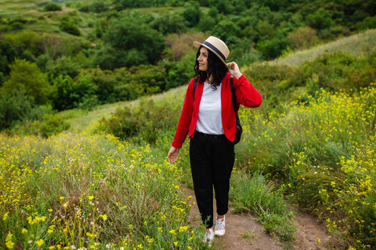 A beautiful girl in a straw hat walks among the hills and fields with flowers. Travel concept.