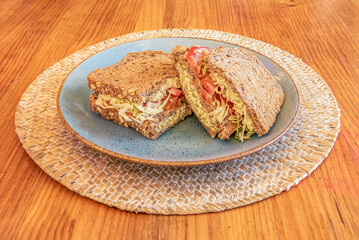 Sandwich of whole wheat bread with seeds and filling to the top of vegetables and lettuce on rattan trivet and wooden table