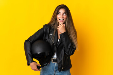 Woman holding a motorcycle helmet isolated on yellow background looking to the side and smiling