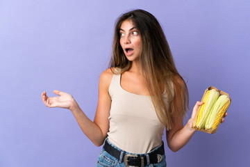 Young woman holding corn isolated on purple background with surprise facial expression