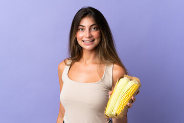 Obraz premium Young woman holding corn isolated on purple background smiling a lot