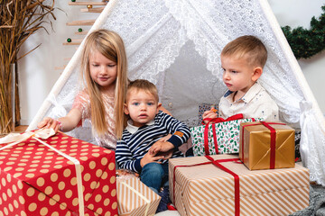 happy children sit between Christmas gift boxes and toys in a decorated house